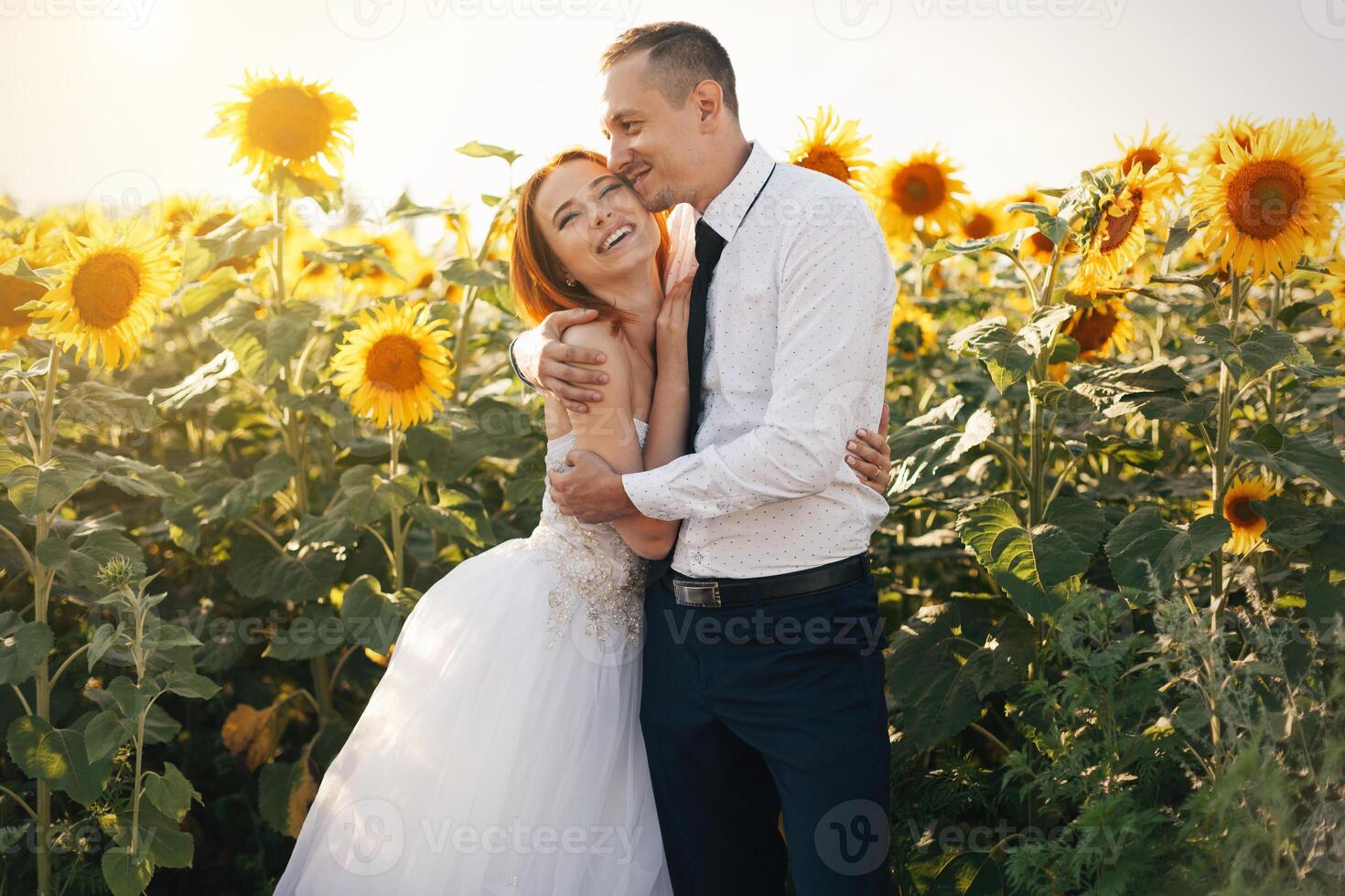 Braut im Hochzeit Weiß Kleider und Bräutigam im weiß Hemd und Krawatte Stehen umarmen im das Feld von Sonnenblumen foto