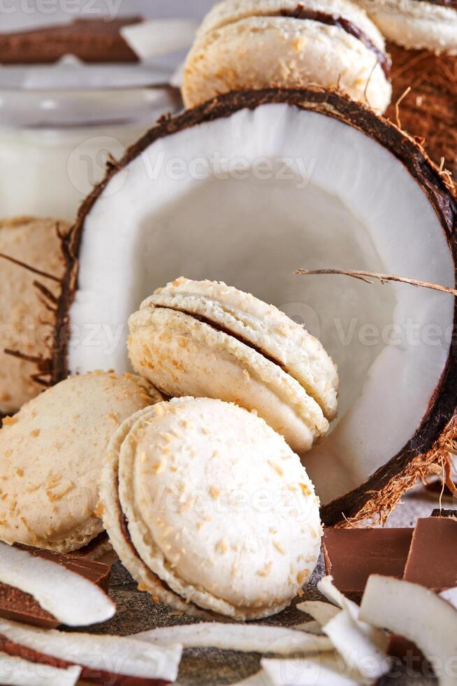 Kokosnuss Macarons mit Schokolade und Kokosnuss Flocken auf ein Tabelle mit ein Kokosnuss im das Hintergrund foto