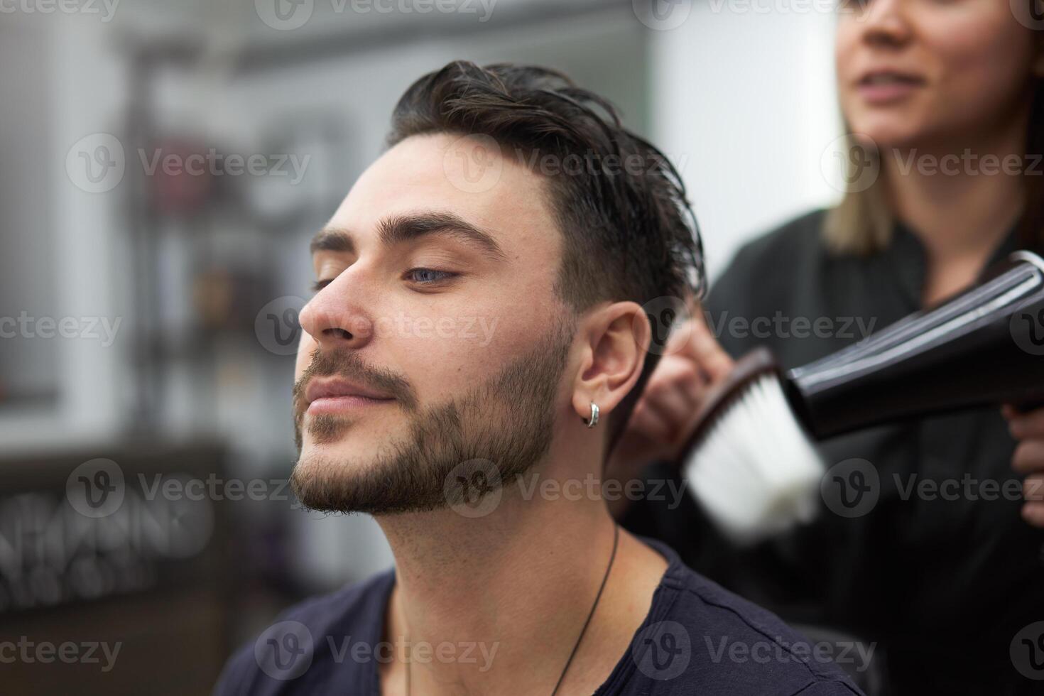 gut aussehend Blau Augen Mann Sitzung im Barbier Geschäft. Friseur Friseur Frau Schneiden seine Haar. weiblich Barbier. foto