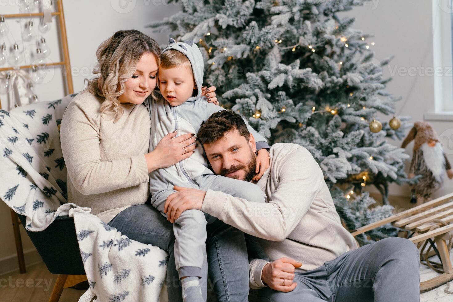 Weihnachten Familie Glück Porträt von Papa, schwanger Mama und wenig Sohn Sitzung Sessel beim Zuhause in der Nähe von Weihnachten Baum Umarmung Lächeln foto