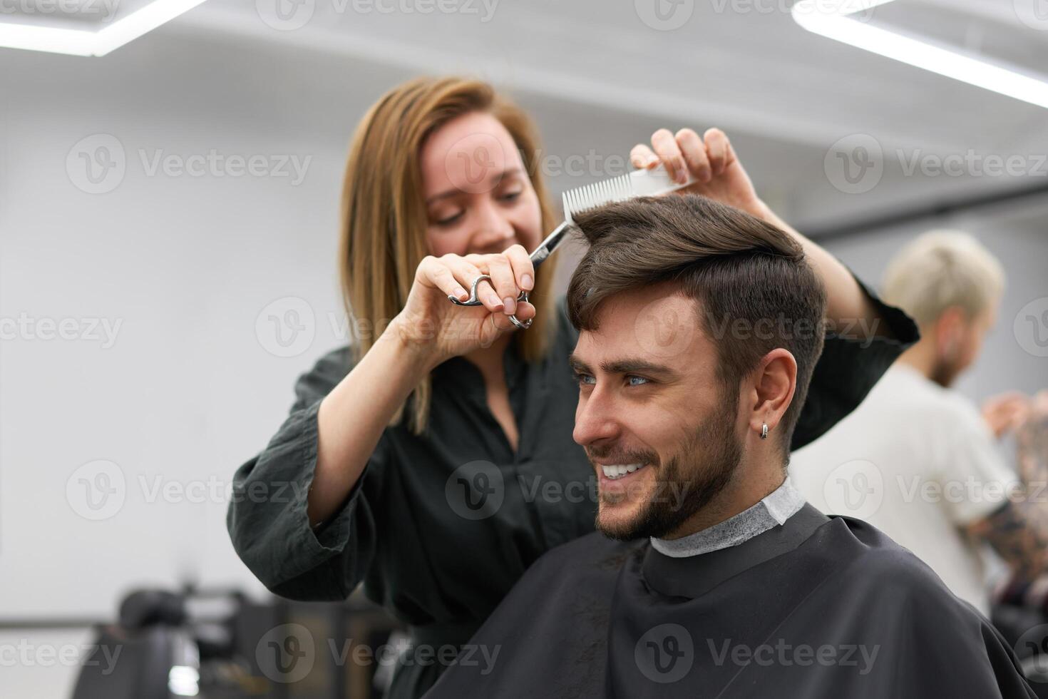 gut aussehend Blau Augen Mann Sitzung im Barbier Geschäft. Friseur Friseur Frau Schneiden seine Haar. weiblich Barbier. foto