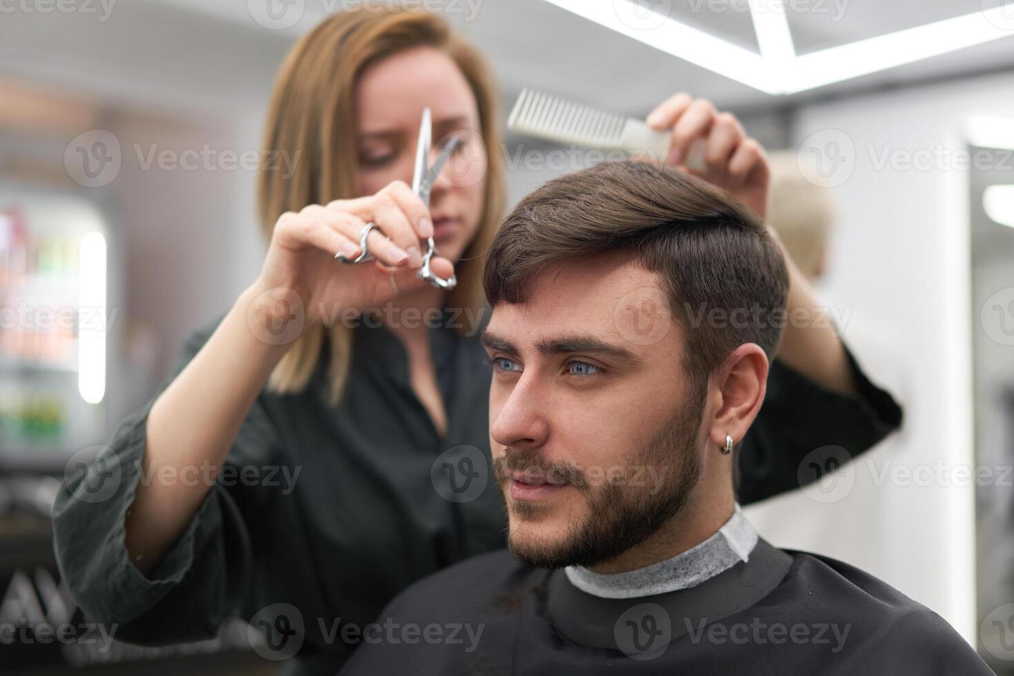 gut aussehend Blau Augen Mann Sitzung im Barbier Geschäft. Friseur Friseur Frau Schneiden seine Haar. weiblich Barbier. foto