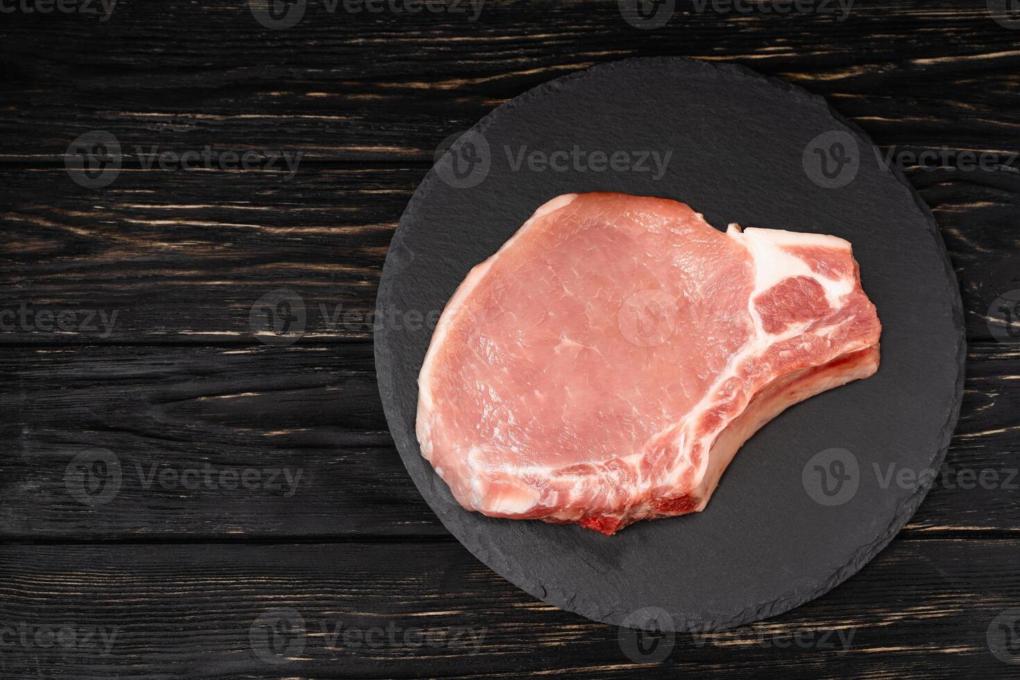 oben Aussicht von einer Stücke roh Schweinefleisch hacken Steaks auf ein schwarz Stein Schneiden Tafel. foto