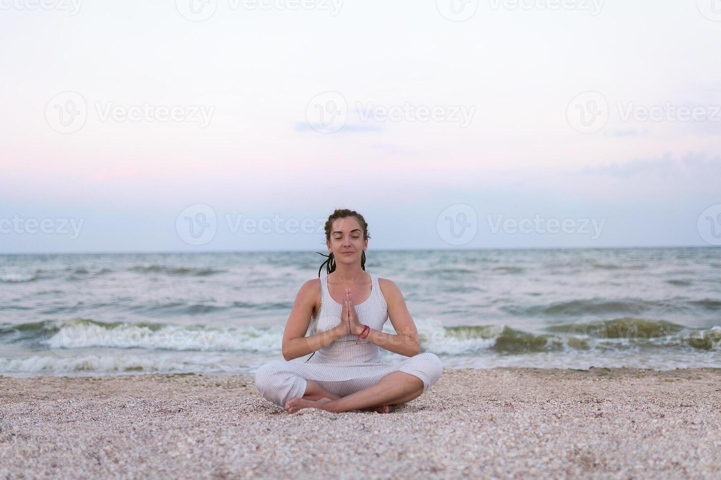 Frau Praktiken Methoden Ausübungen Yoga und meditiert im das Lotus Position auf das Strand foto