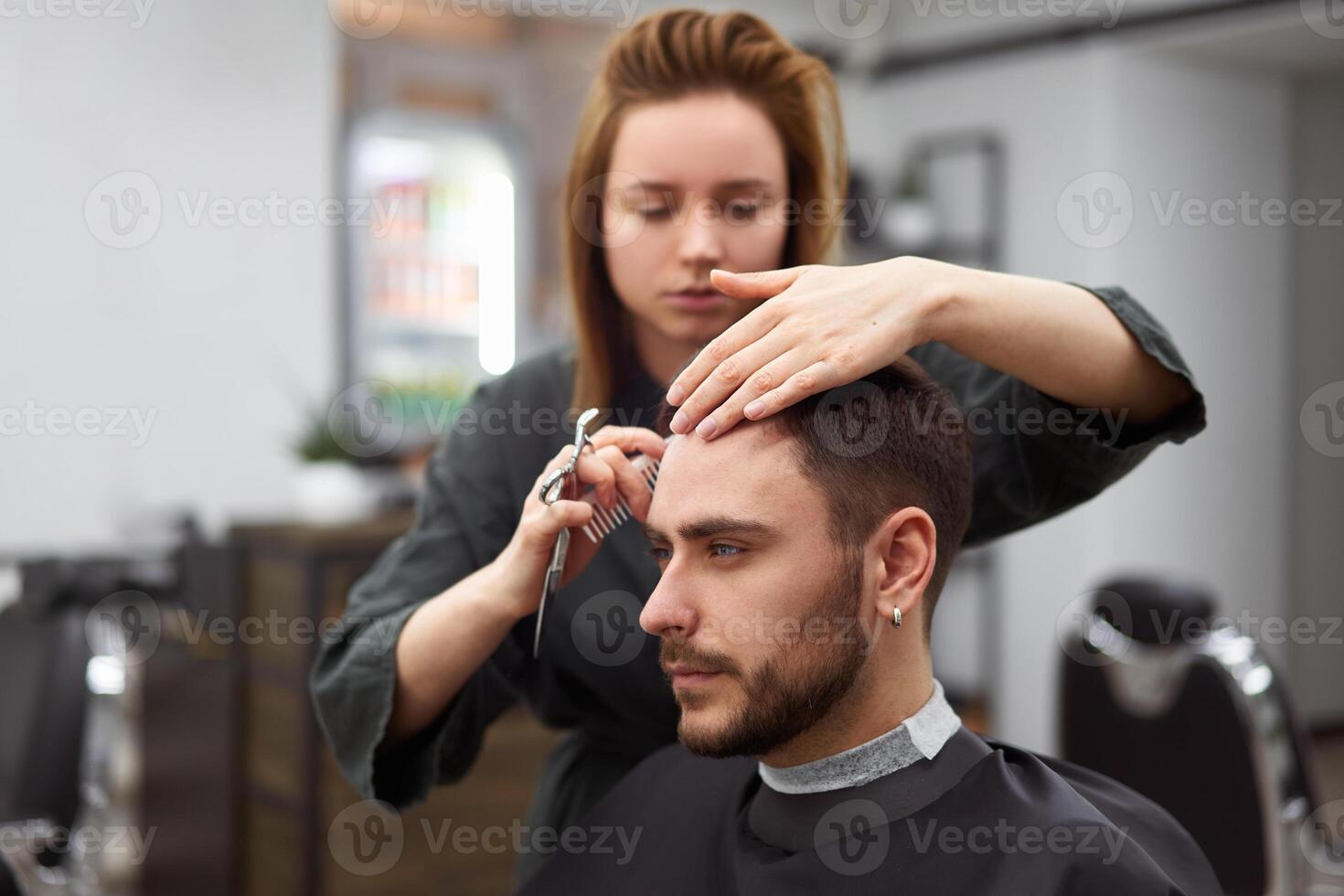 gut aussehend Blau Augen Mann Sitzung im Barbier Geschäft. Friseur Friseur Frau Schneiden seine Haar. weiblich Barbier. foto