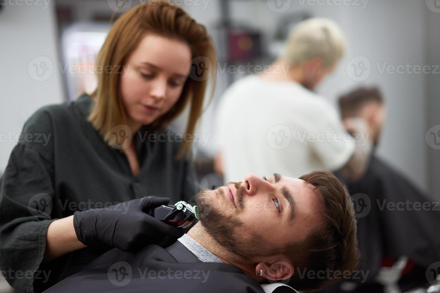 jung schön kaukasisch Frau Friseur schneidet Bart gut aussehend Mann beim modern Friseur foto