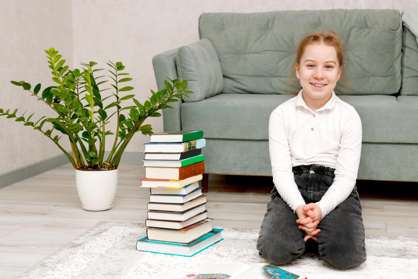 lächelnd Mädchen Sitzung auf das Fußboden Nächster zu ein Stapel von Bücher beim Zuhause foto