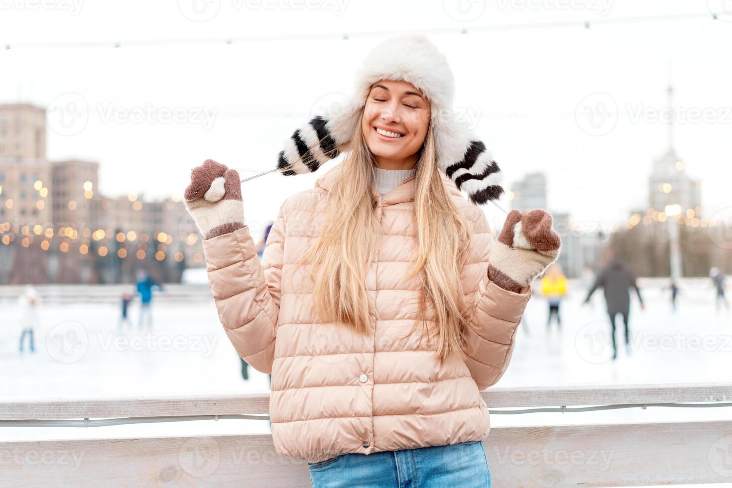 Mittel schießen Porträt von romantisch europäisch Dame trägt lange stilvoll Winter Jacke und komisch flauschige Hut im schneebedeckt Tag. draussen Foto von inspiriert blond Frau genießen Winter Stadt.