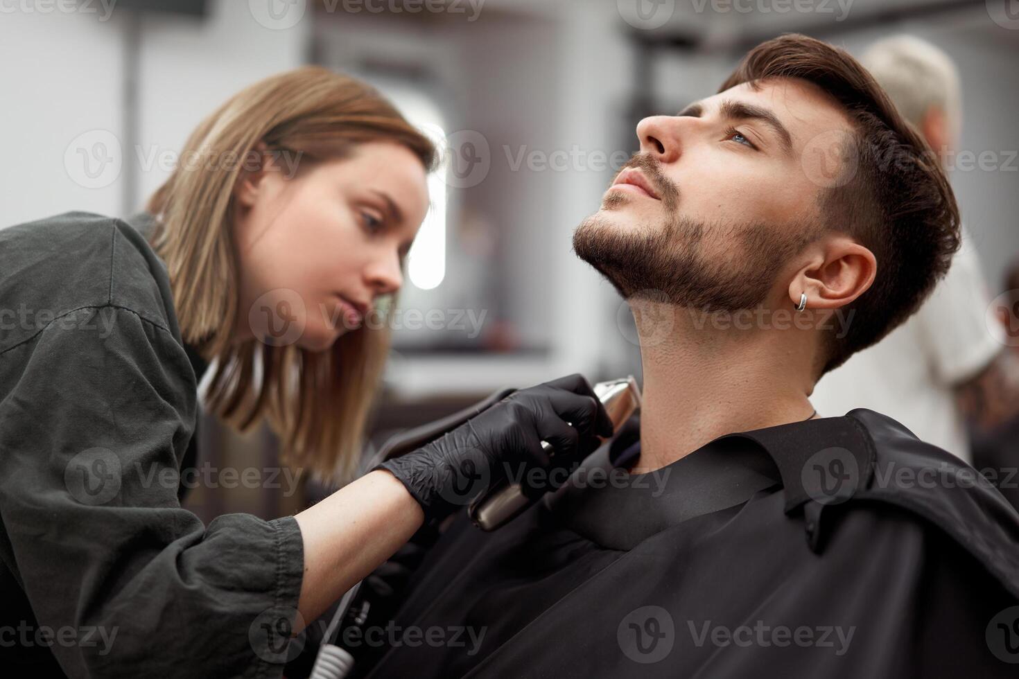 jung schön kaukasisch Frau Friseur schneidet Bart gut aussehend Mann beim modern Friseur foto