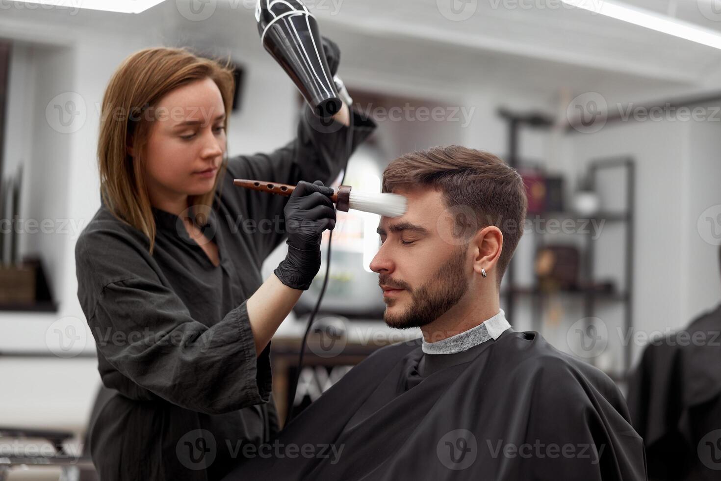 gut aussehend Blau Augen Mann Sitzung im Barbier Geschäft. Friseur Friseur Frau Schneiden seine Haar. weiblich Barbier. foto