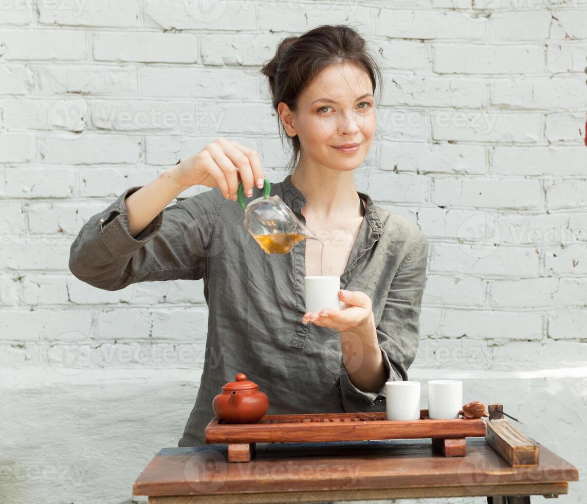 orientalisch Meister von Tee Zeremonie mit Weiß Backstein Mauer auf das Hintergrund. traditionell Tee Party auf das Natur mit Frau gekleidet im das grau Hemd foto