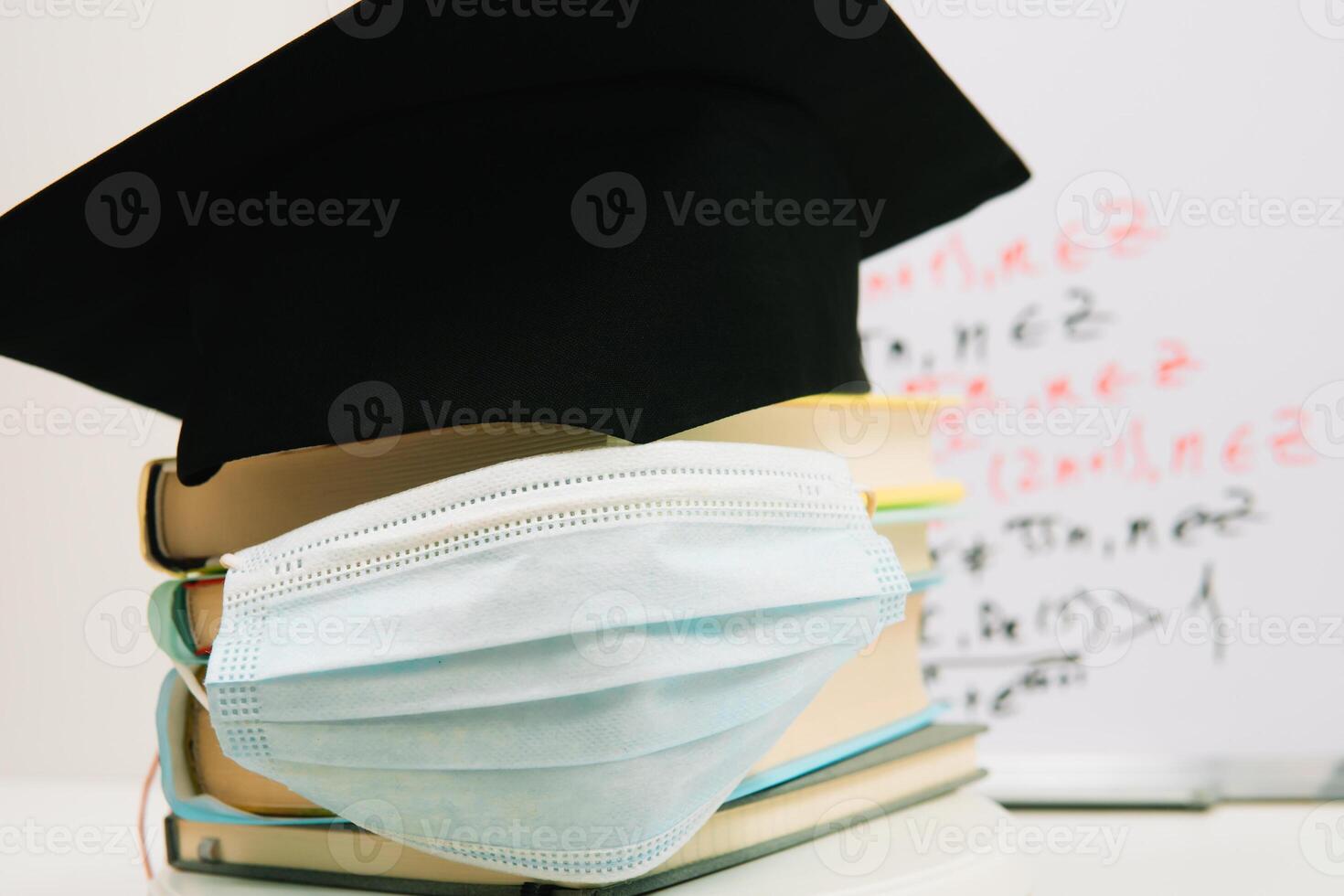 das schwarz Platz Hut von das Meister Lügen auf das Lehrbücher gestapelt im ein Säule und dekoriert mit ein schützend medizinisch Maske. Bildung Konzept foto