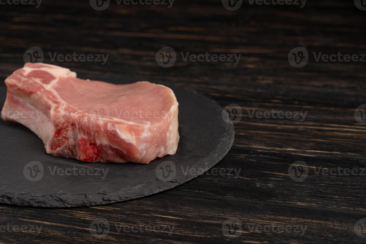 oben Aussicht von einer Stücke roh Schweinefleisch hacken Steaks auf ein schwarz Stein Schneiden Tafel. foto