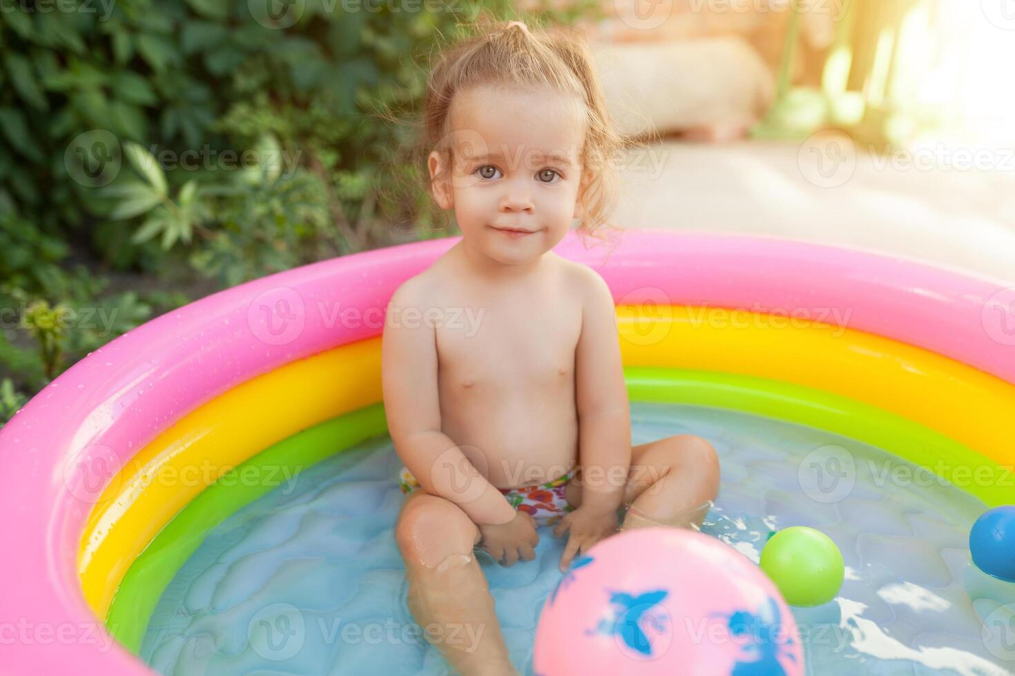 Kinder spielen im aufblasbar Baby Schwimmbad. Kinder schwimmen und Spritzen im bunt Garten abspielen Center. glücklich wenig Mädchen spielen mit Wasser Spielzeuge auf heiß Sommer- Tag. Familie haben Spaß draußen im das Hinterhof. foto