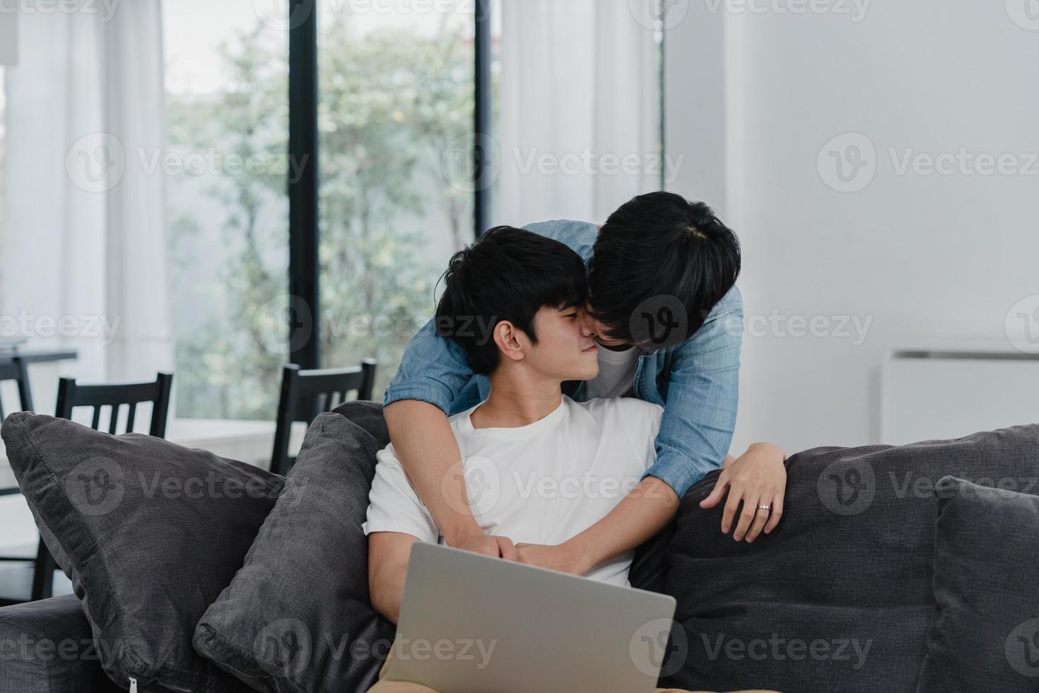 junges schwules Paar mit Computer-Laptop im modernen Zuhause. asiatische lgbtq-männer glücklich entspannen spaß mit technologie, die zusammen filme im internet ansehen, während sie im wohnzimmer auf dem sofa im hauskonzept liegen. foto