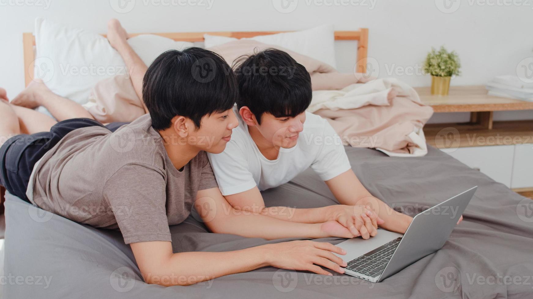asiatische schwule lgbtq-männer paar mit computer-laptop im modernen haus. Junge asiatische Liebhaber männlich glücklich entspannen sich nach dem Aufwachen zusammen und schauen sich am Morgen einen Film auf dem Bett im Schlafzimmer im Haus an. foto