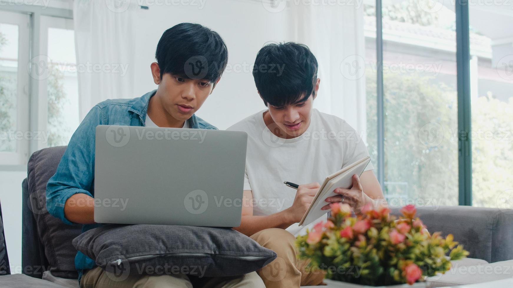 junges asiatisches schwules Paar, das Laptop im modernen Zuhause arbeitet. asia lgbtq männer glücklich entspannen spaß mit computer und analysieren ihre finanzen im internet zusammen, während sie auf dem sofa im wohnzimmer im hauskonzept liegen. foto