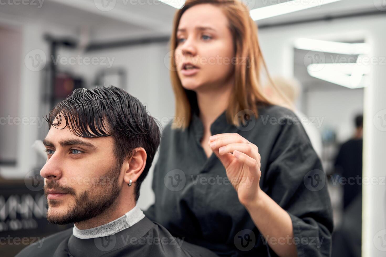 gut aussehend Blau Augen Mann Sitzung im Barbier Geschäft. Friseur Friseur Frau Schneiden seine Haar. weiblich Barbier. foto