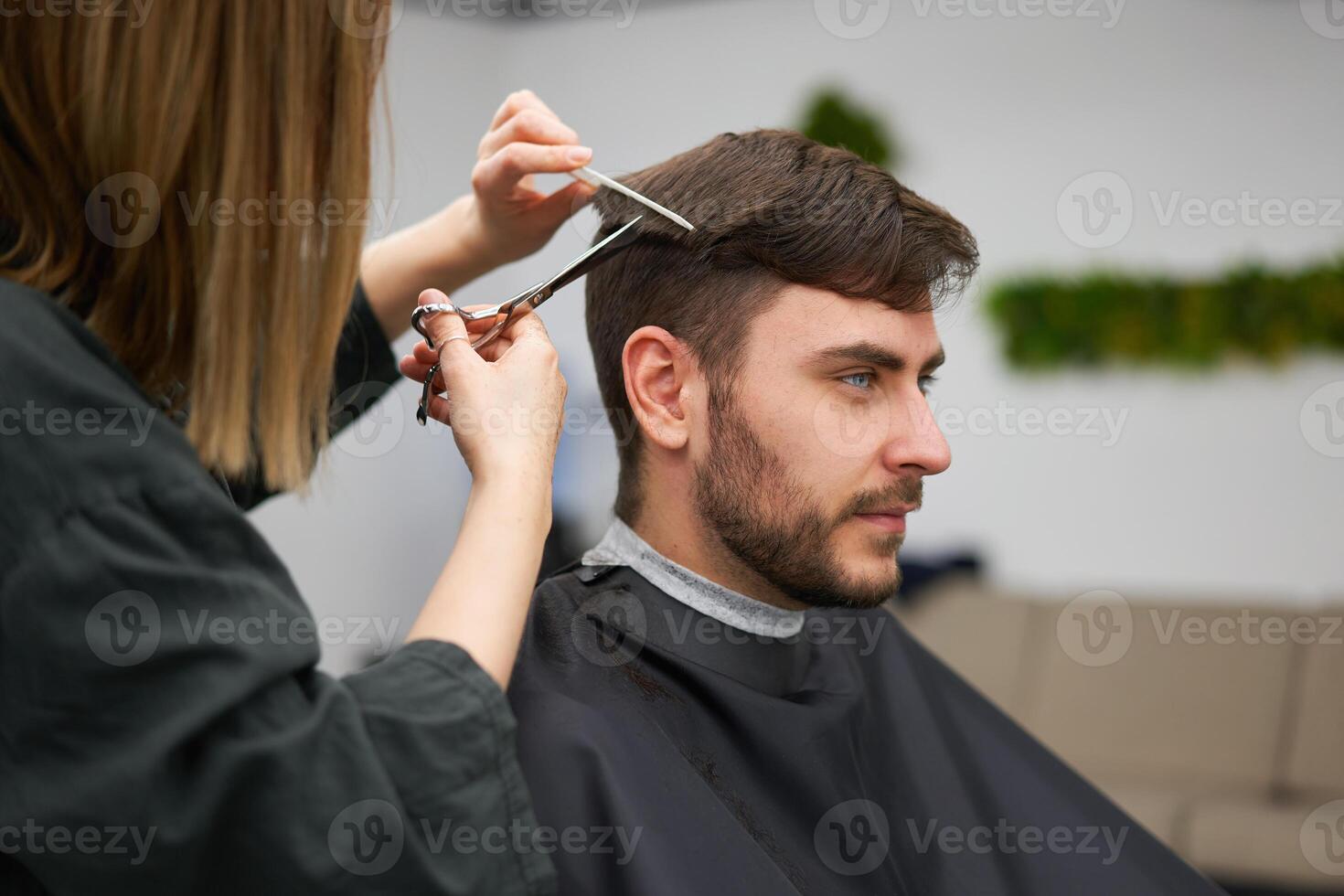 gut aussehend Blau Augen Mann Sitzung im Barbier Geschäft. Friseur Friseur Frau Schneiden seine Haar. weiblich Barbier. foto