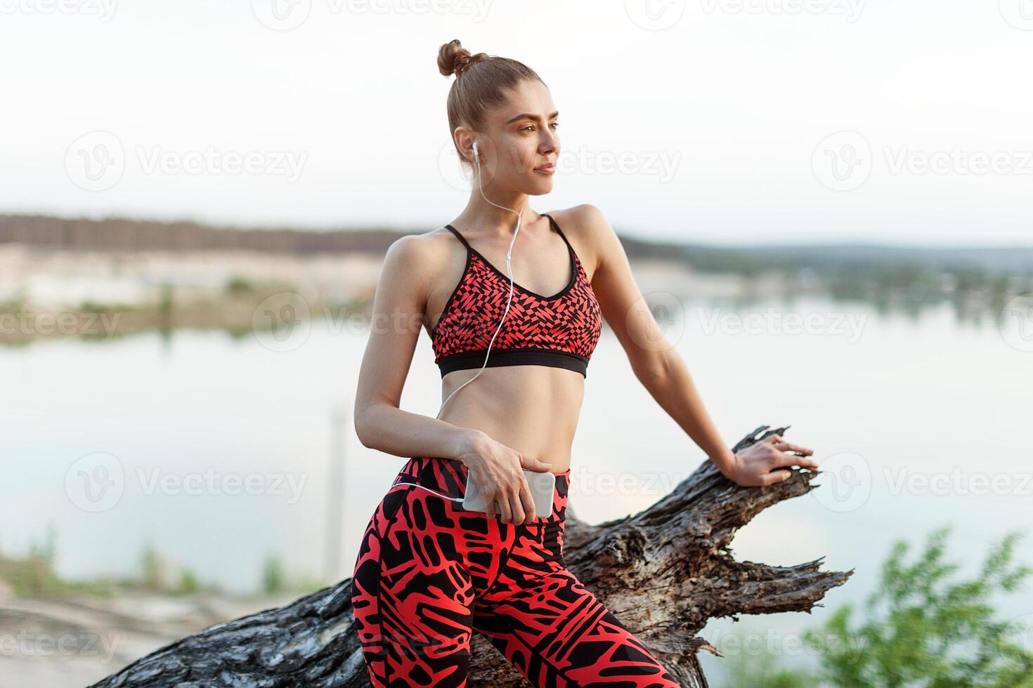 ein schön Brünette Mädchen im stilvoll Sport Kleider ist ruhen nach ein Sport aktiv trainieren in der Nähe von das See. foto