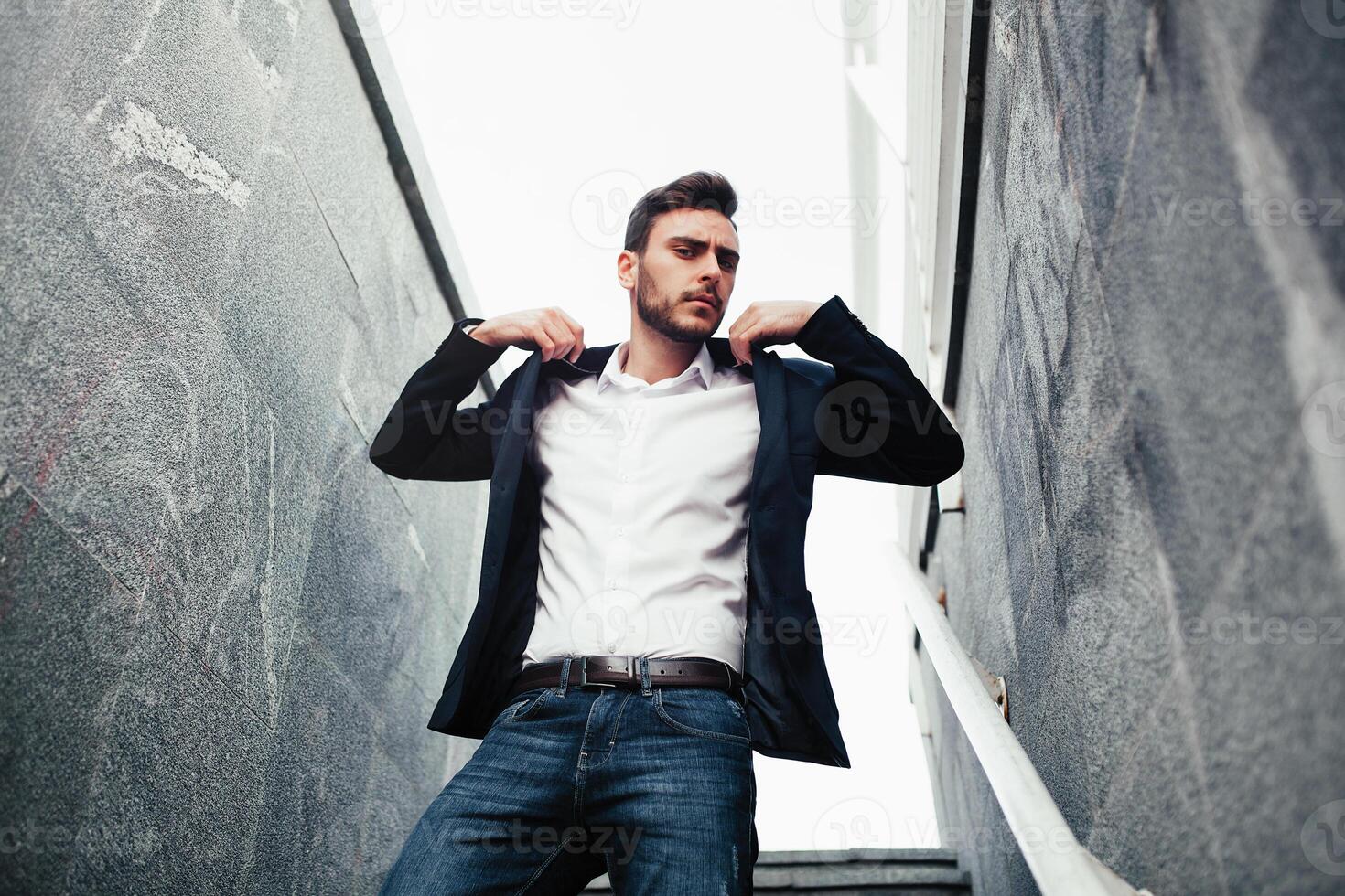 jung stilvoll Geschäftsmann Mann mit ein Bart im ein modisch passen und Jeans. modern Bild von Geschäft Jugend. es steht auf das Hintergrund von Marmor Wände foto