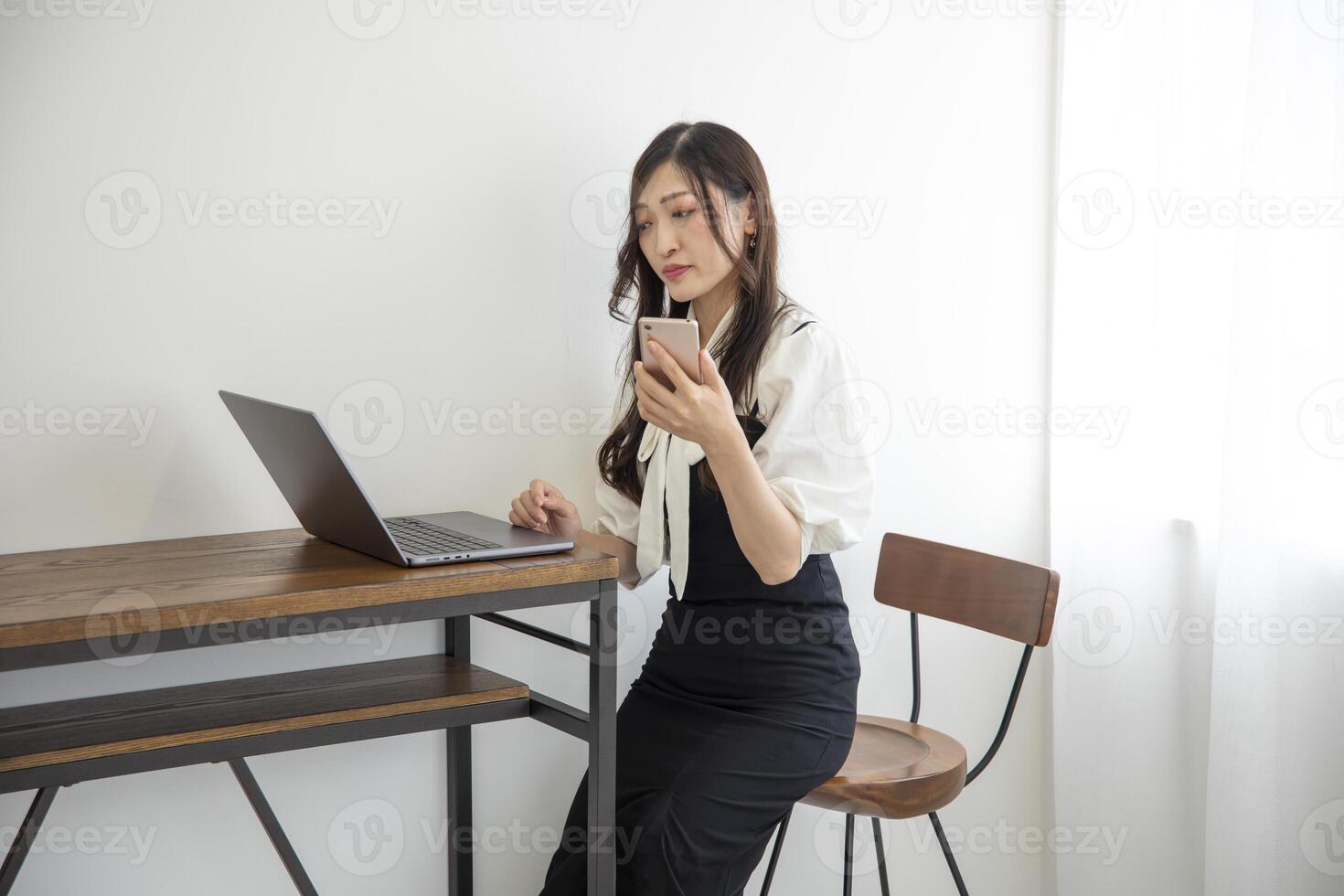 ein japanisch Frau Überprüfung Smartphone durch Fernbedienung Arbeit im das Zuhause Büro foto