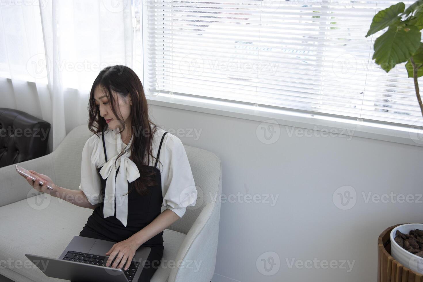 ein japanisch Frau Überprüfung Smartphone durch Fernbedienung Arbeit im das Zuhause Büro foto