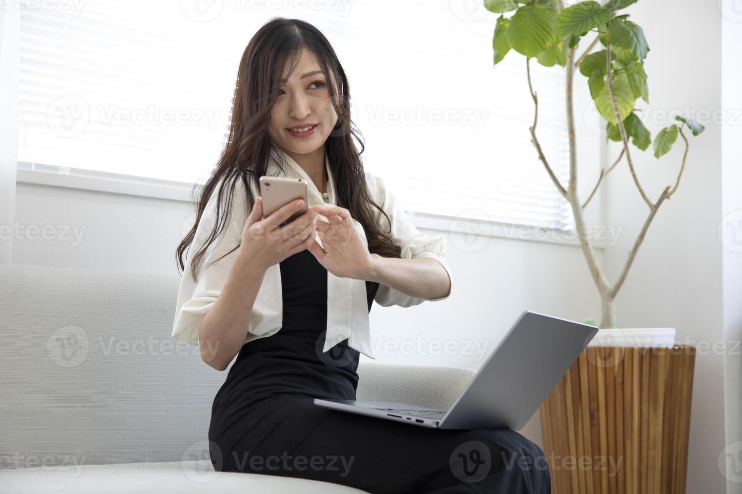 ein japanisch Frau Überprüfung Smartphone durch Fernbedienung Arbeit im das klein Büro foto