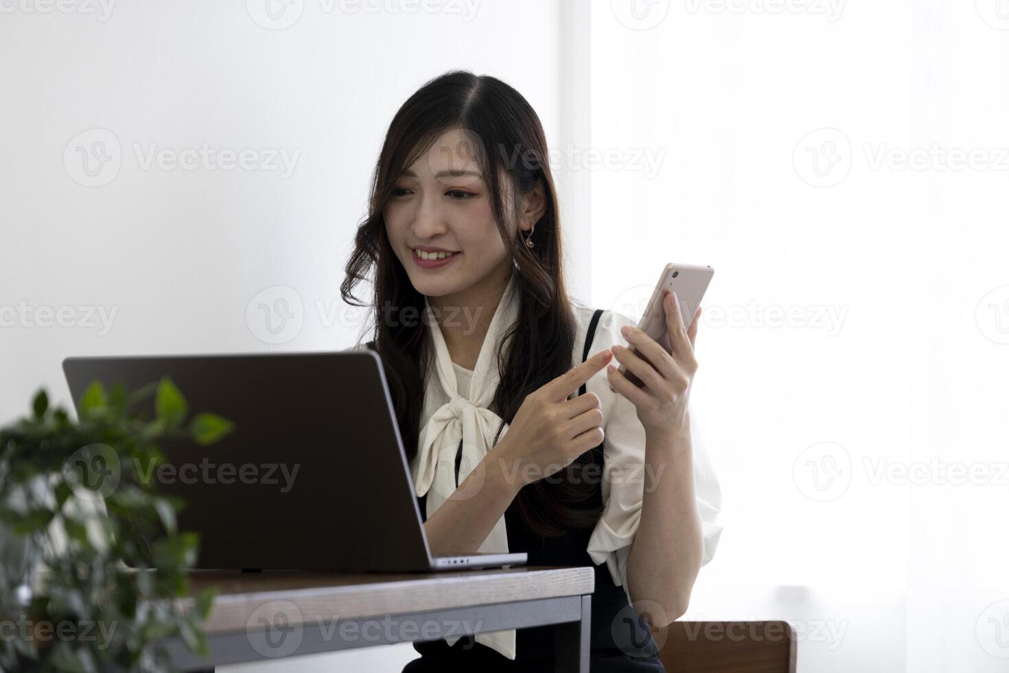 ein japanisch Frau Überprüfung Smartphone durch Fernbedienung Arbeit im das klein Büro foto