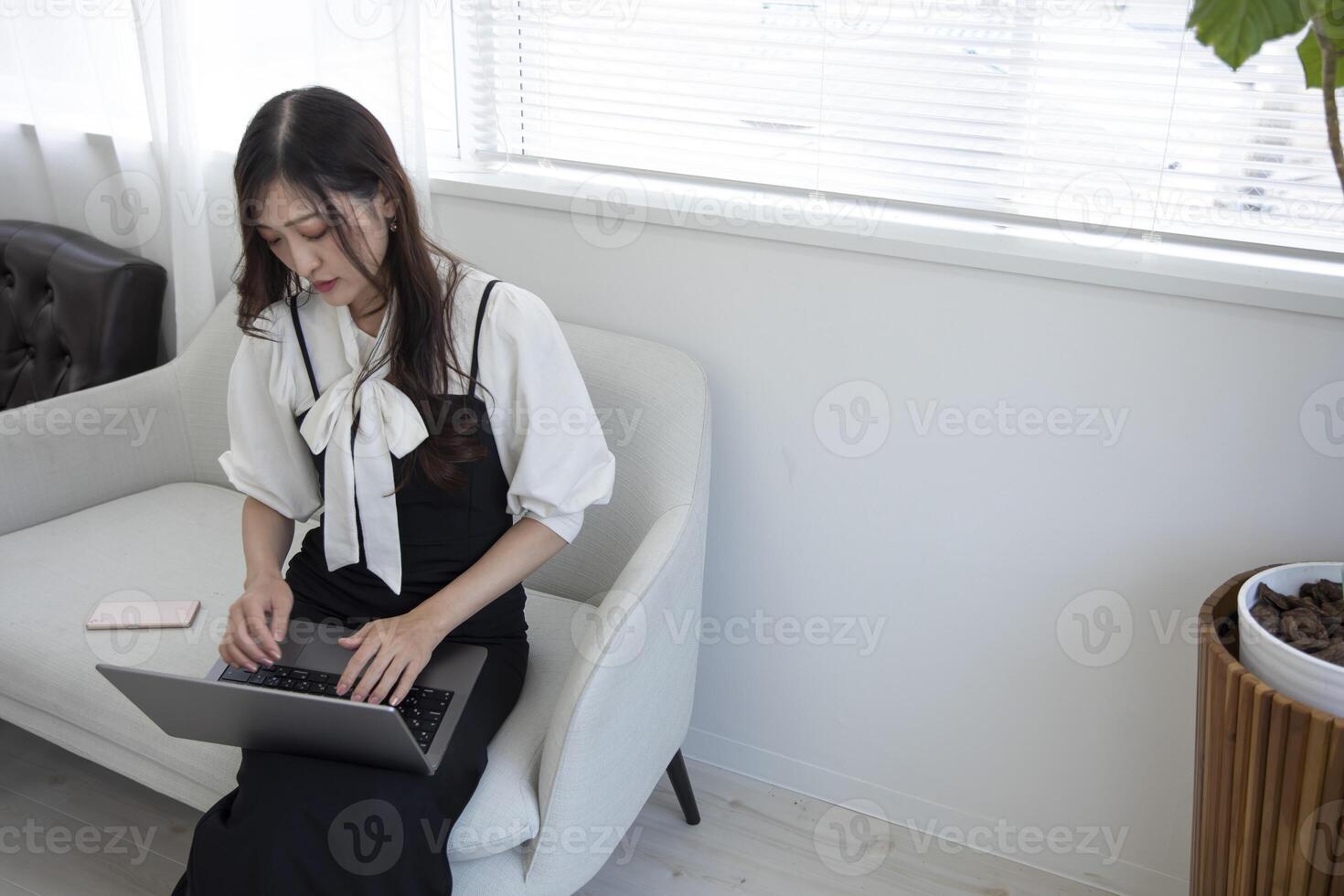 ein japanisch Frau Überprüfung Smartphone durch Fernbedienung Arbeit im das Zuhause Büro foto