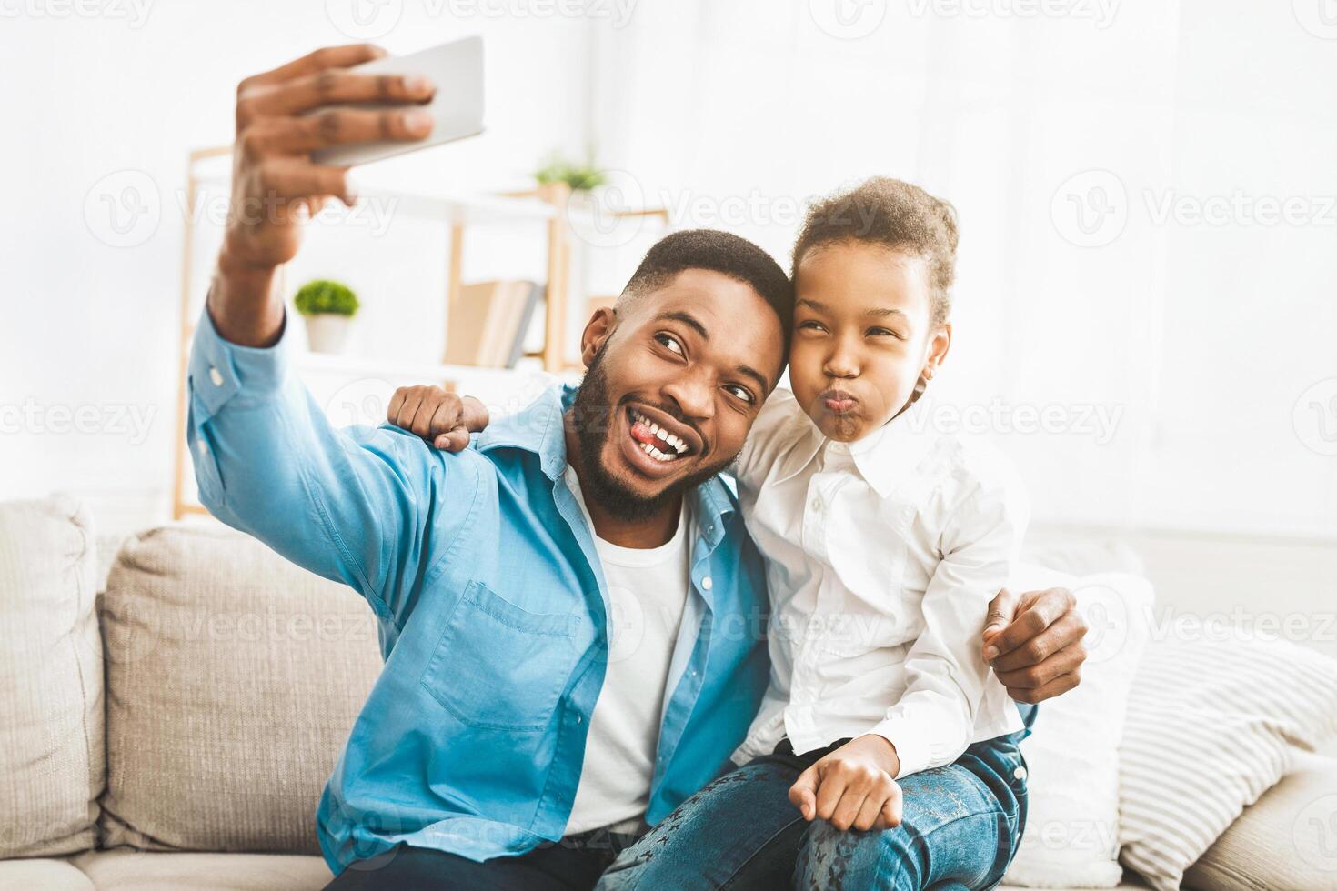 glücklich afro Vater nehmen Selfie mit seine komisch Tochter foto