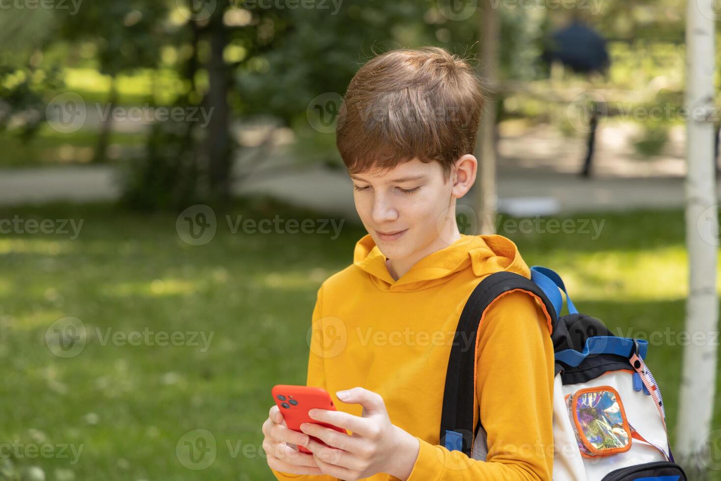 jung Junge mit gekleidet Gelb Kapuzenpullover suchen beim seine Handy, Mobiltelefon Telefon, draußen Frühling Zeit. foto