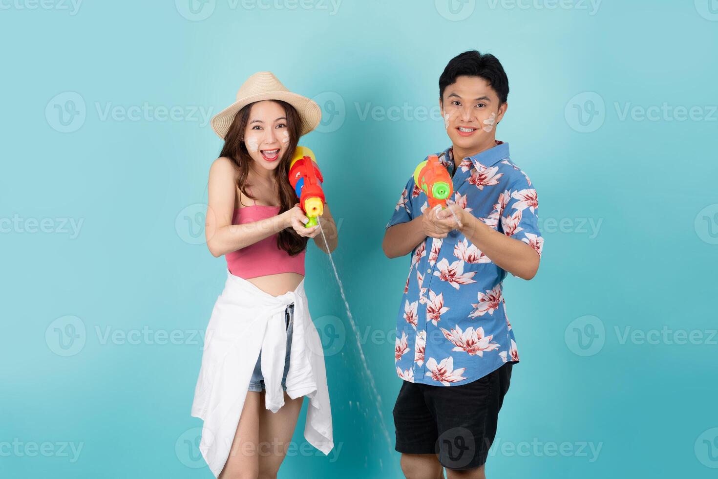 Porträt von ein asiatisch Tourist spielen im das Wasser mit ein Plastik Wasser Gewehr auf ein Blau Hintergrund mit Kopieren Raum. Songkran Festival foto