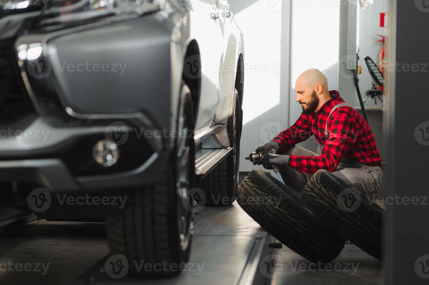 Mechaniker Ändern ein Auto Reifen im ein Werkstatt auf ein Fahrzeug auf ein hissen mit ein elektrisch bohren zu lösen das Schrauben im ein Konzept von Bedienung oder Ersatz foto