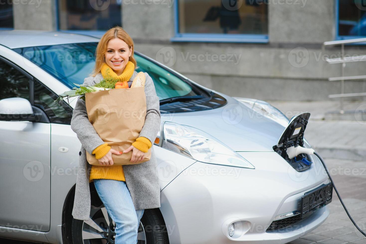 stilvoll Frau nach Kauf Produkte mit ein Einkaufen Tasche ist Stehen in der Nähe von das Laden elektrisch Wagen. foto