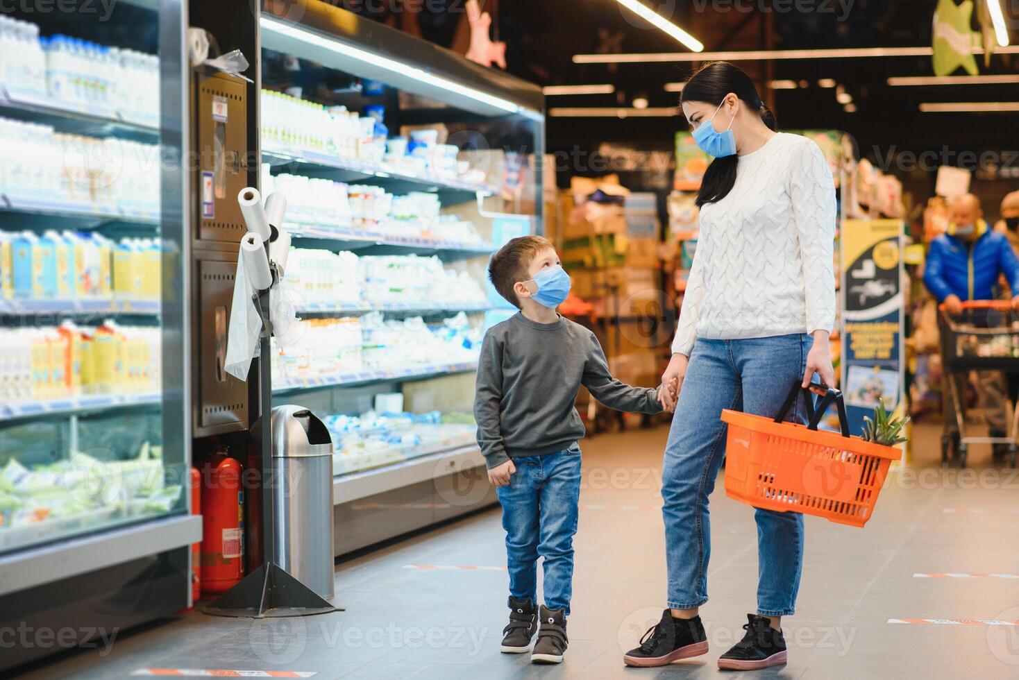 Einkaufen mit Kind während Virus Ausbruch. Mutter und Kind tragen chirurgisch Gesicht Maske Kauf Obst im Supermarkt. Mama und wenig Junge Kaufen frisch Gemüse im Lebensmittelgeschäft speichern. Familie im Geschäft foto
