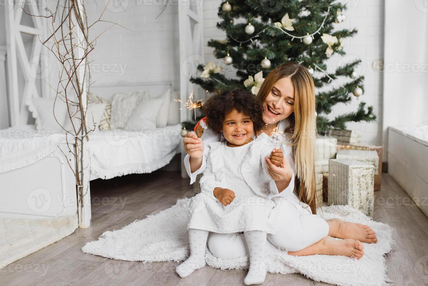 fröhlich Weihnachten und glücklich Ferien heiter Mama und ihr süß Tochter beim Weihnachten Baum. Elternteil und wenig Kind haben Spaß in der Nähe von Weihnachten Baum drinnen. liebend Familie mit die Geschenke im Zimmer. foto