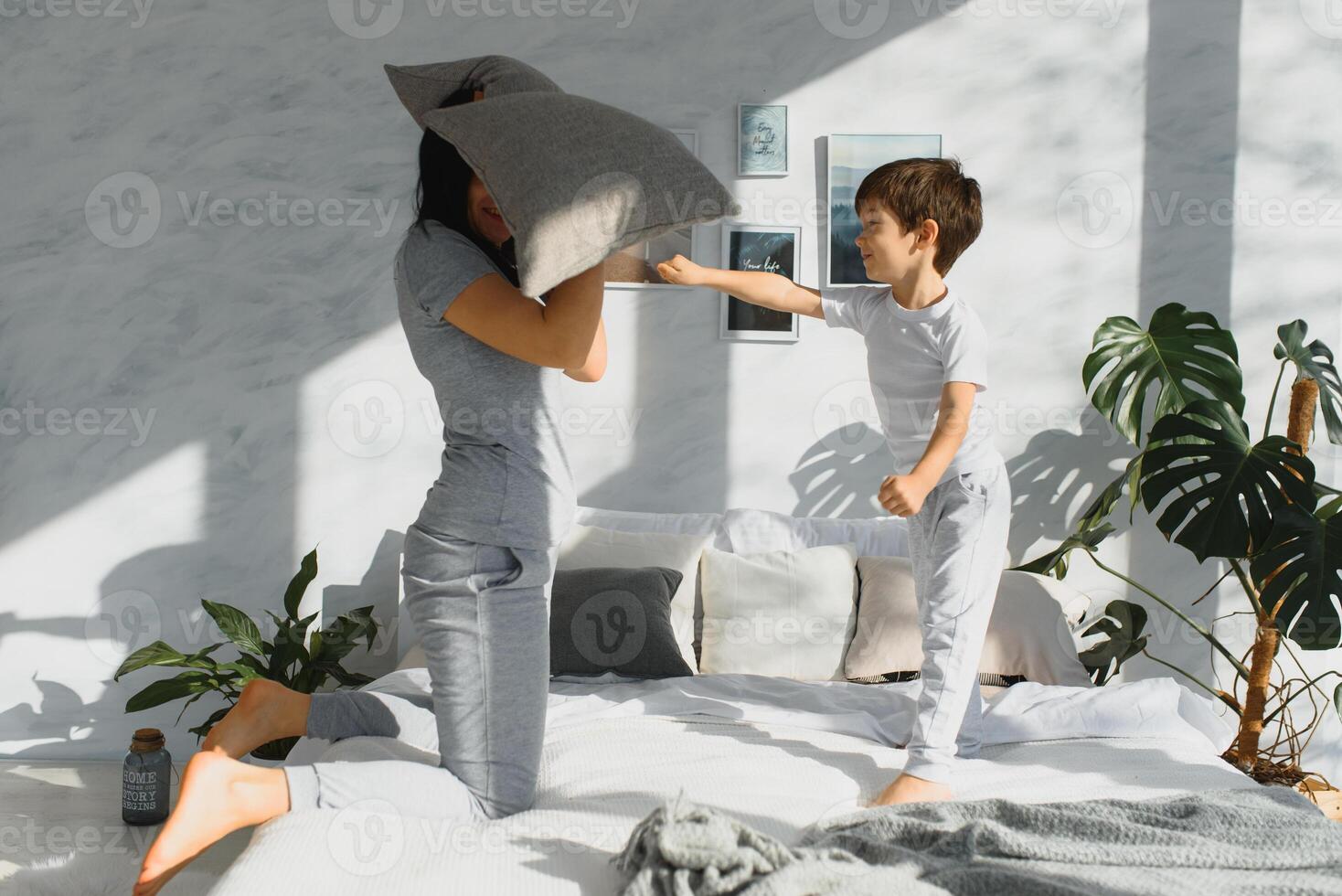 Mama und Sohn Lachen und spielen auf das Bett, haben ein Kissen Kampf im das Morgen während tragen Pyjama. Familie beiläufig Lebensstil Serie. foto