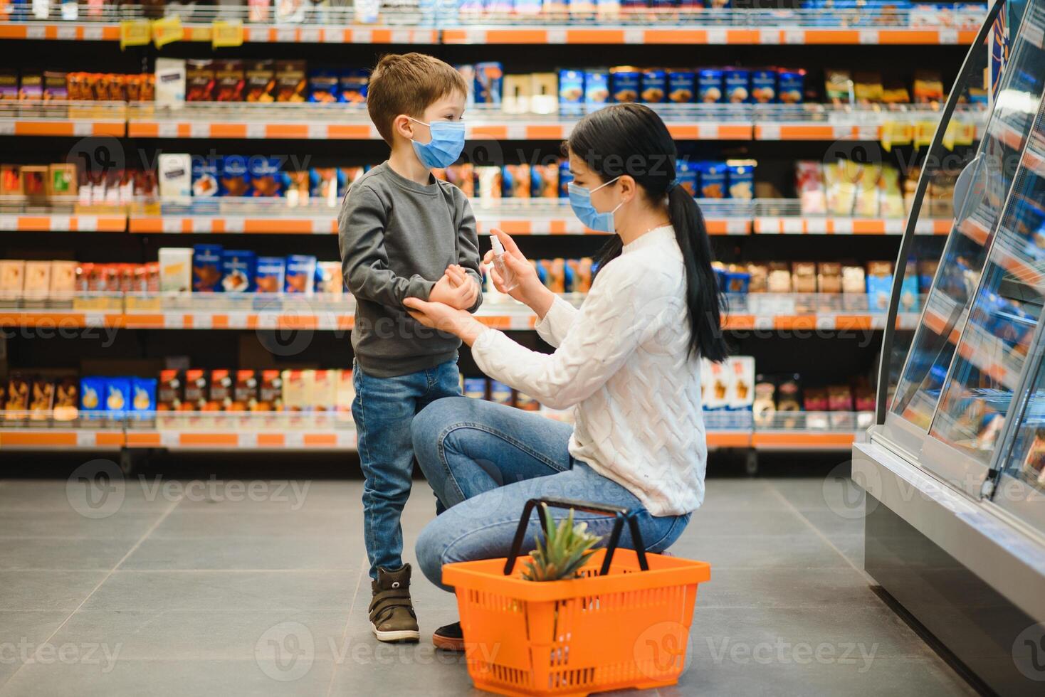 Mutter gilt Desinfektionsmittel zum Reinigung Söhne Hände im Öffentlichkeit überfüllt Ort. Einkaufen Einkaufszentrum foto