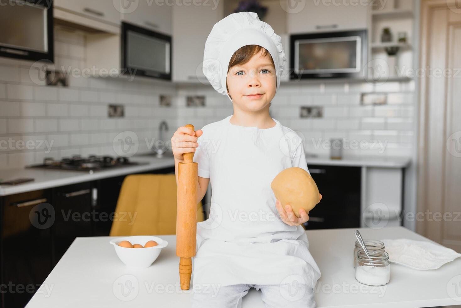 Junge im Koch Hut Sitzung beim ein Küche Schalter. wenig Junge im Küche foto