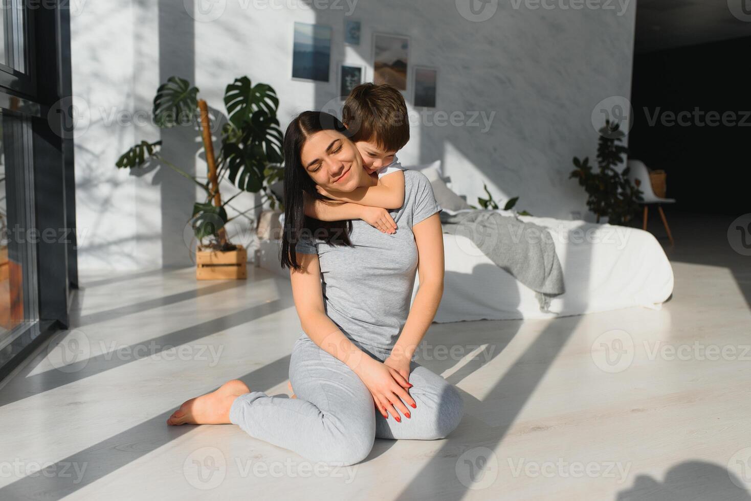 Mama ist umarmen ihr Sohn Sitzung auf das Fußboden im das Zimmer. Familie Zuhause schießen. foto