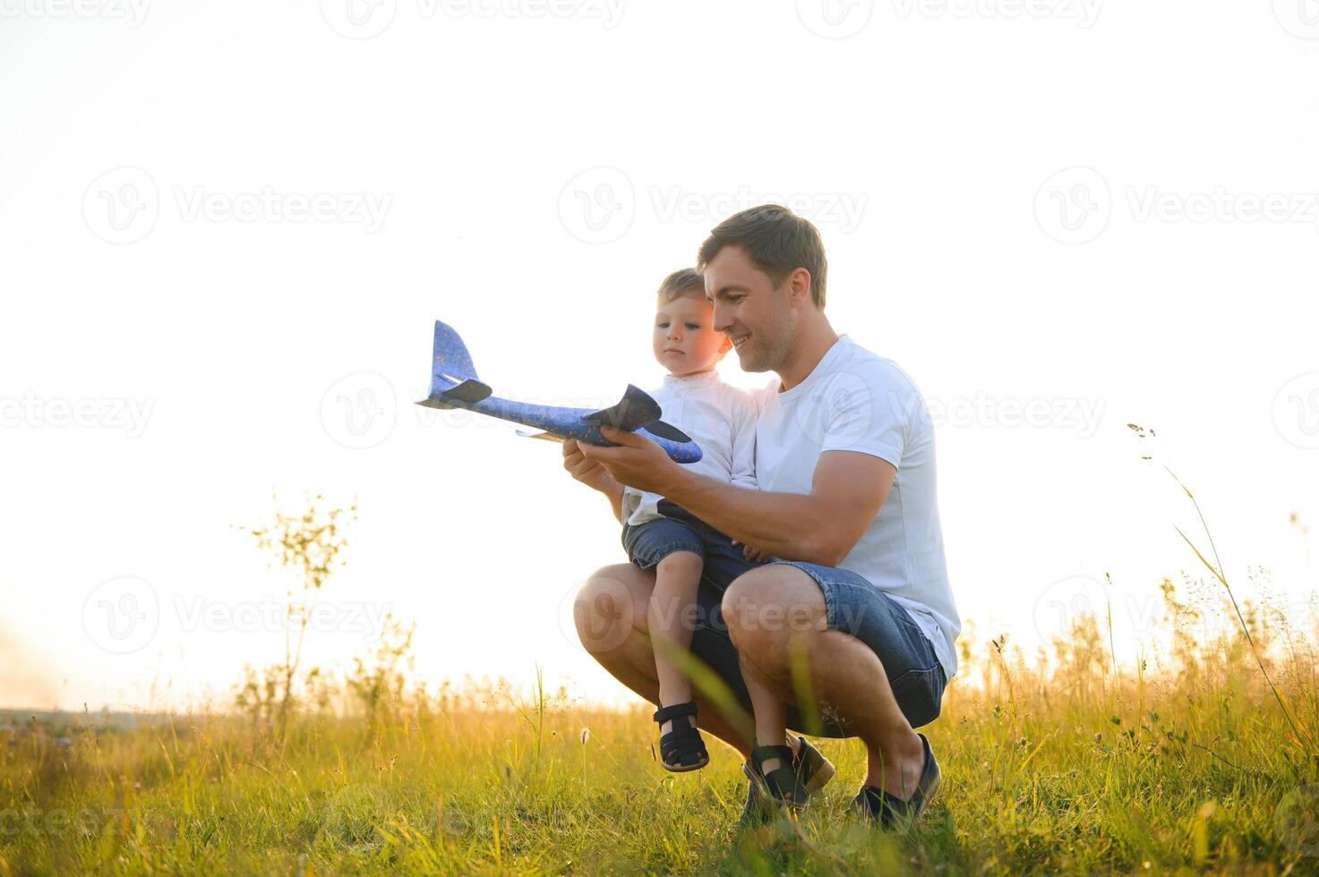 süß wenig Junge und seine gut aussehend jung Papa sind lächelnd während spielen mit ein Spielzeug Flugzeug im das Park. foto