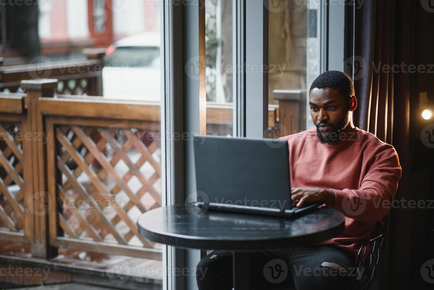 Porträt von glücklich afrikanisch Geschäftsmann mit Telefon während Arbeiten auf Laptop im Restaurant. foto