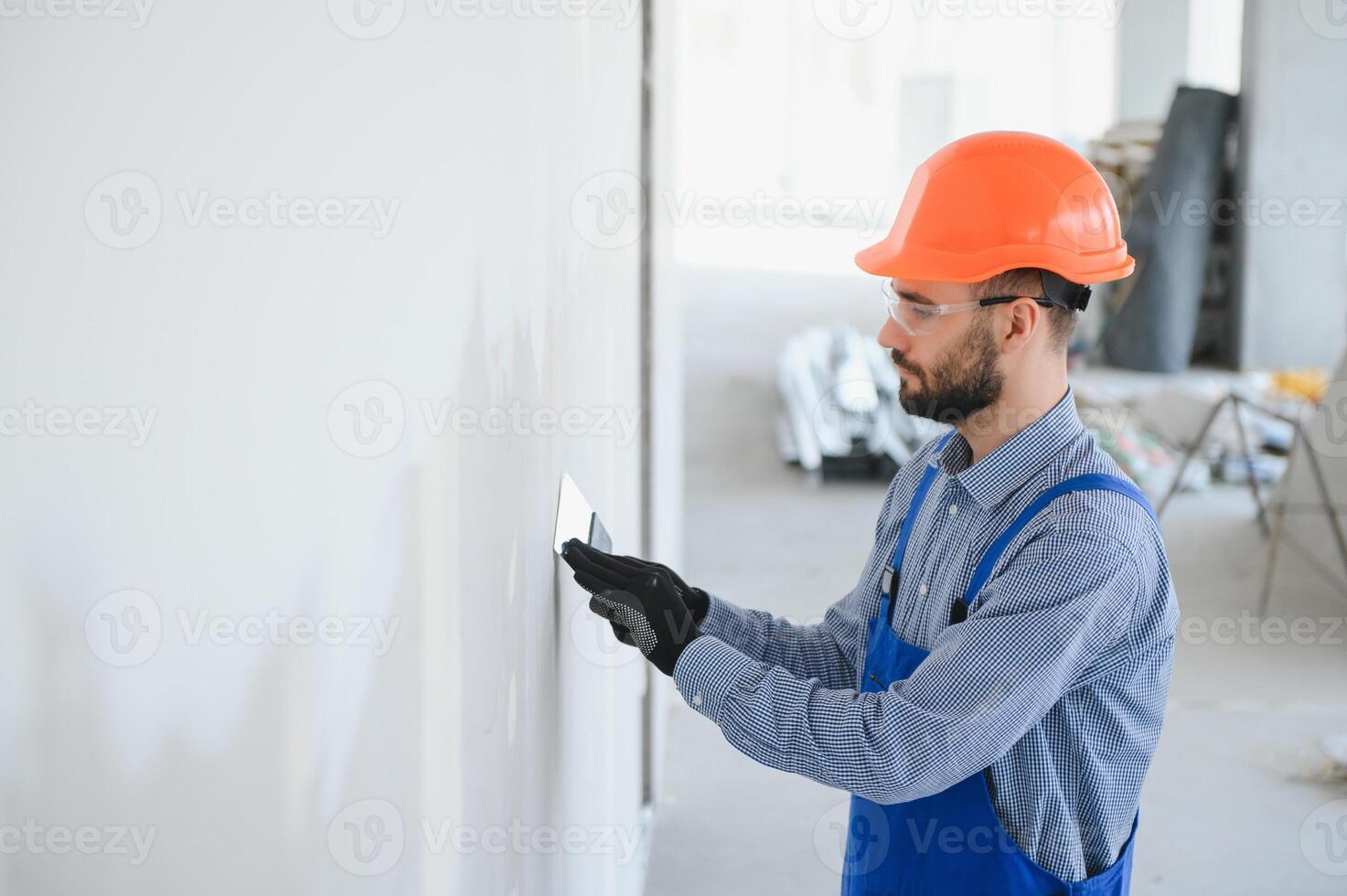 Mann Trockenbau Arbeiter oder Stuckateur Schleifen und Glätten ein Gipskarton Wände mit Stuck mit ein Sandpapier Halter. tragen Weiß Helm und Sicherheit Brille. Panorama- Bild mit Kopieren Raum foto