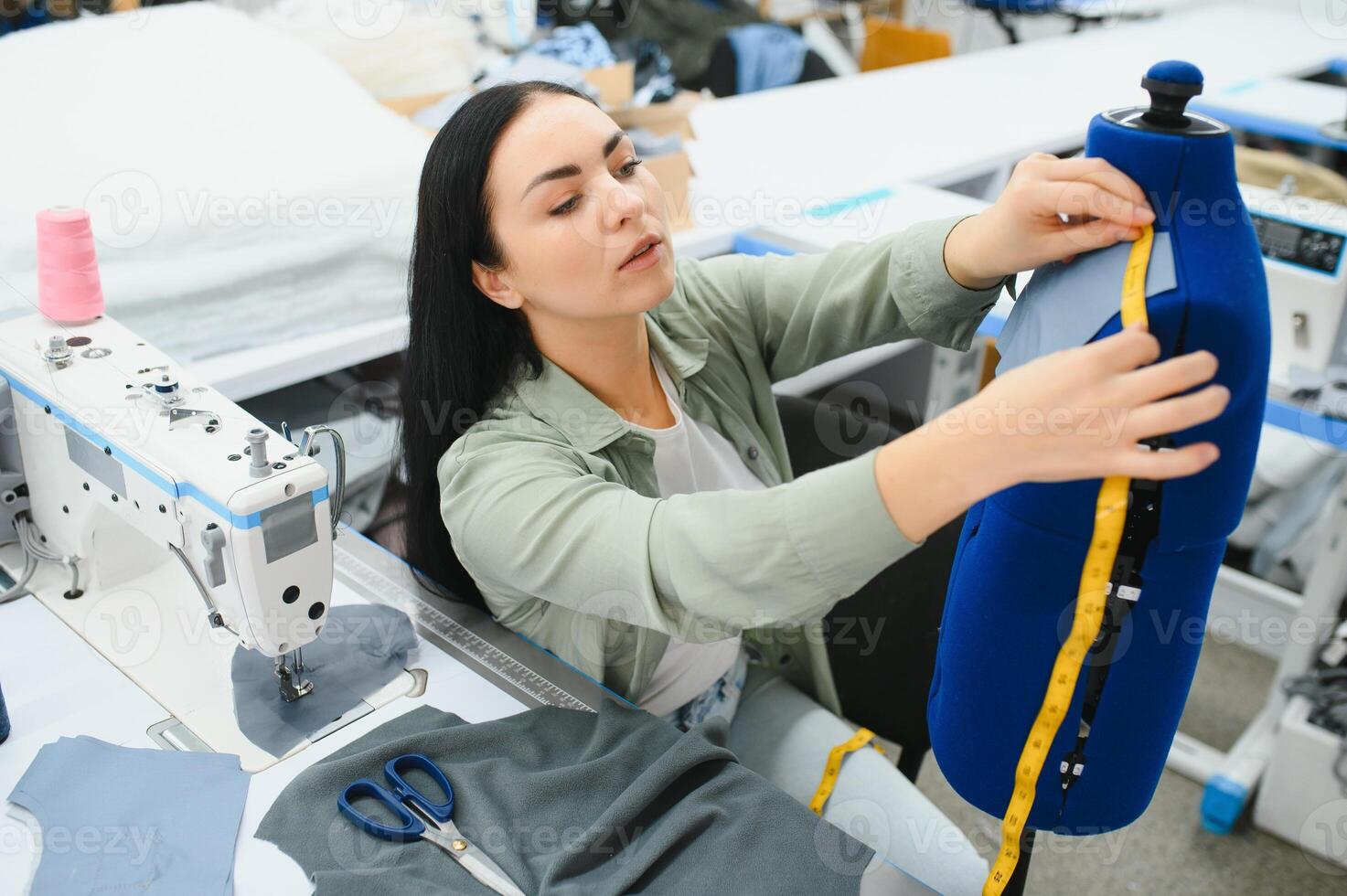 jung Schneider Frau näht Kleider auf Arbeiten Tisch. lächelnd Näherin und ihr Hand schließen oben im Werkstatt. foto