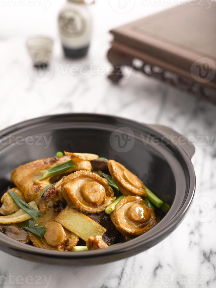 geschmort Hähnchen und Abalone mit Abalone Soße serviert im Kasserolle serviert im ein Topf Seite Aussicht auf grau Hintergrund foto