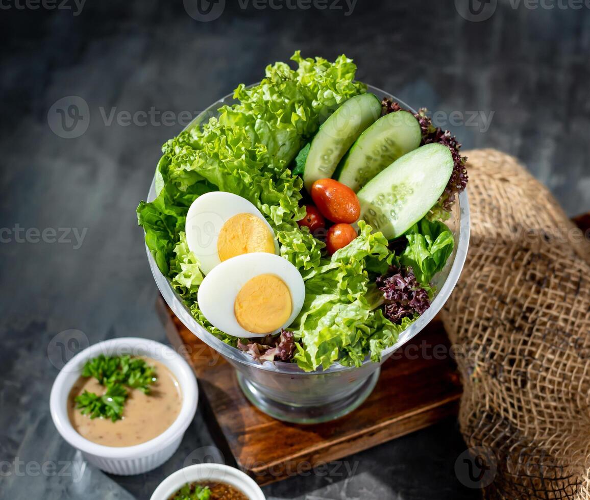 frisch Grüns Salat mit gekocht Ei, Soße und tauchen im ein Schüssel oben Aussicht auf dunkel Hintergrund foto