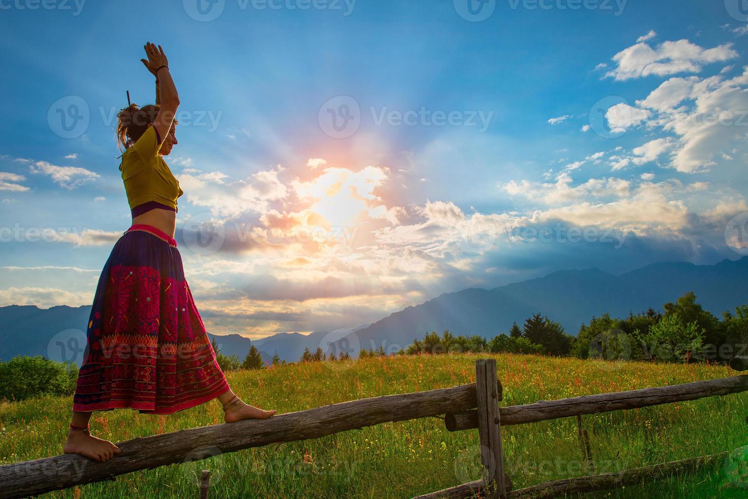 lässiges Mädchen entspannt sich beim Dehnen und Yoga allein in den Bergen über einem Zaun in einer schönen Frühlingswiese. foto