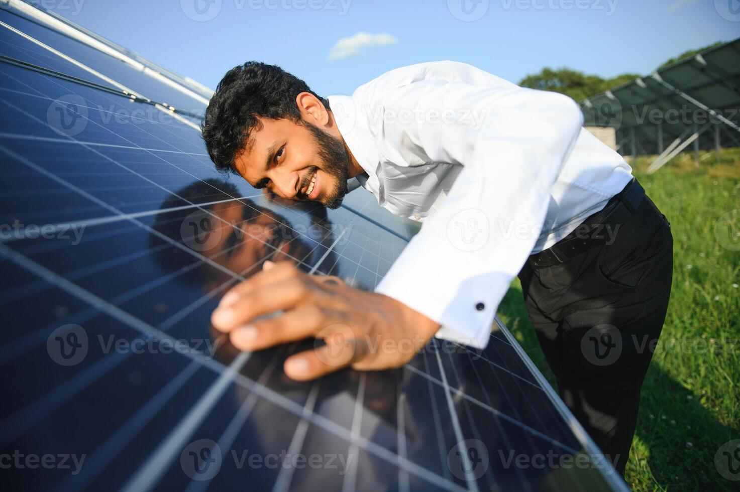 Porträt von jung indisch männlich Ingenieur Stehen in der Nähe von Solar- Tafeln, mit klar Blau Himmel Hintergrund, verlängerbar und sauber Energie. Fertigkeit Indien, Kopieren Raum. foto
