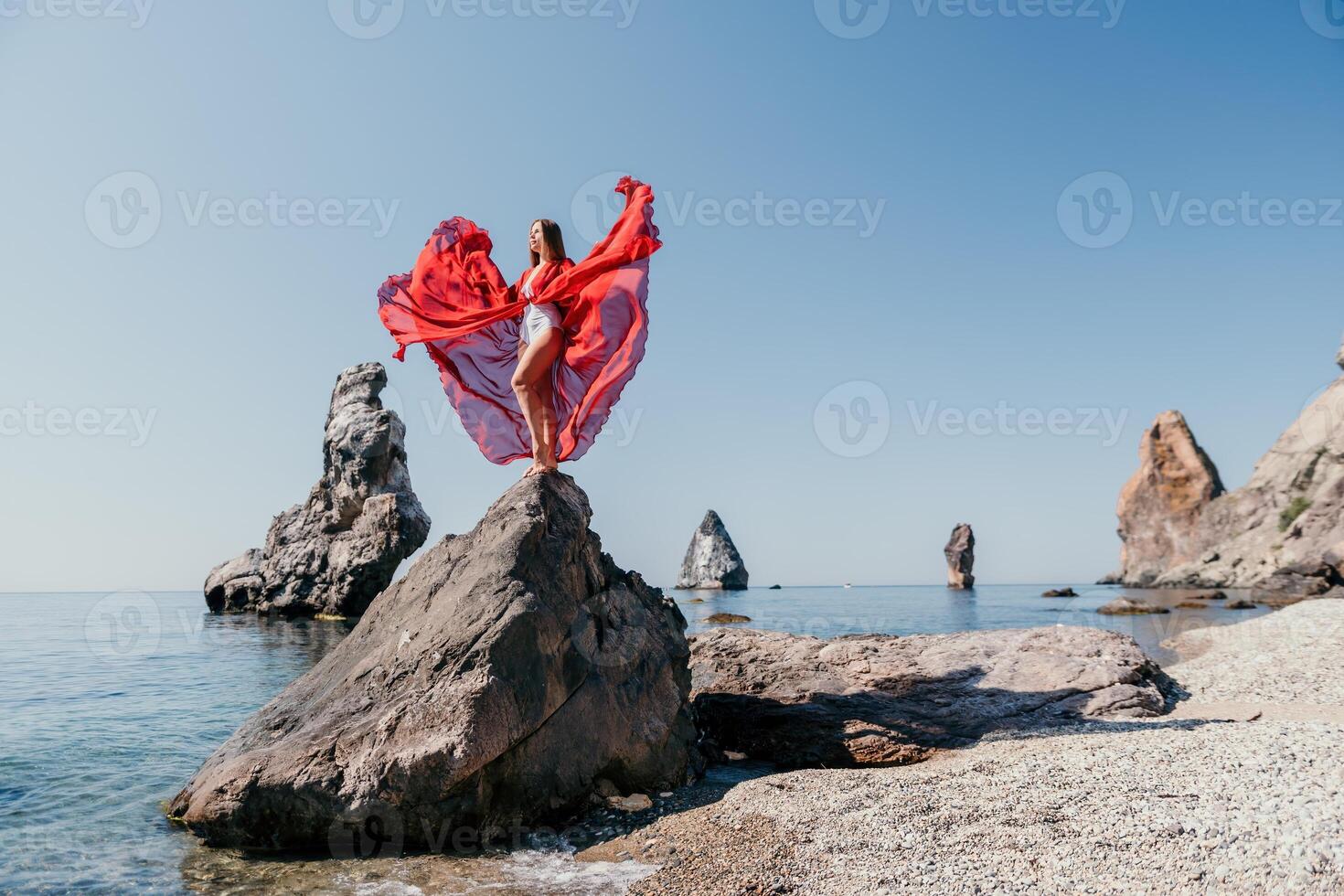 Frau Reise Meer. jung glücklich Frau im ein lange rot Kleid posieren auf ein Strand in der Nähe von das Meer auf Hintergrund von vulkanisch Felsen, mögen im Island, Teilen Reise Abenteuer Reise foto